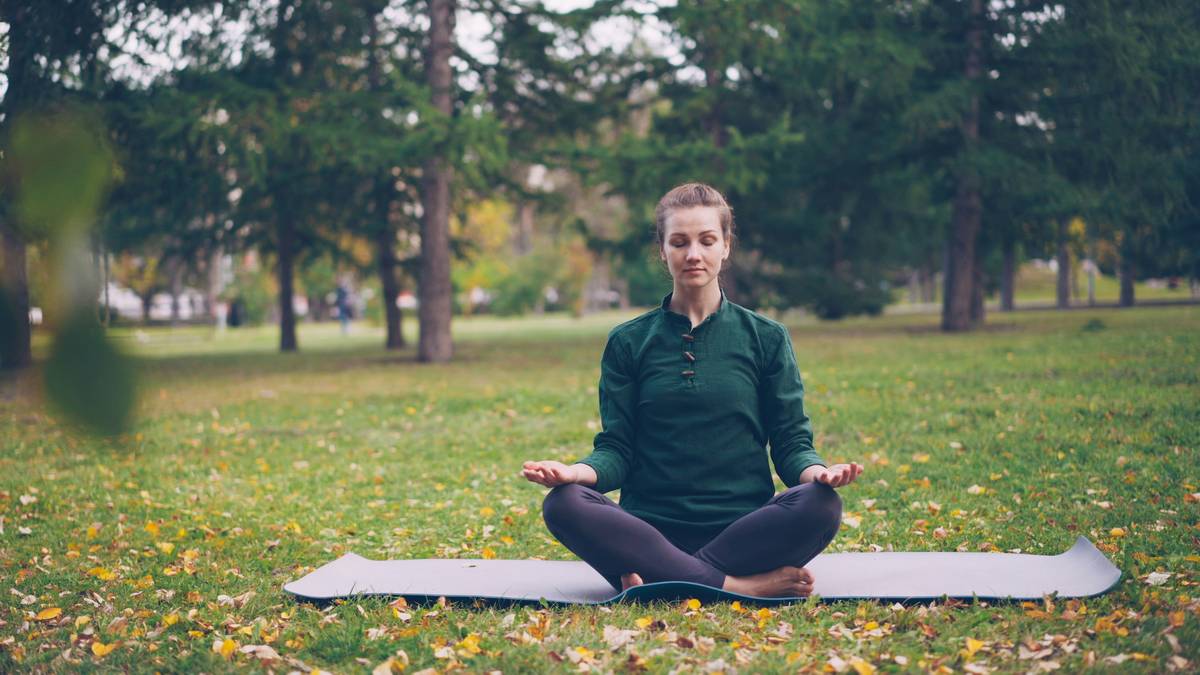 Woman practicing breathing exercises for anxiety while sitting calmly on a park bench, eyes closed, hands resting on her abdomen